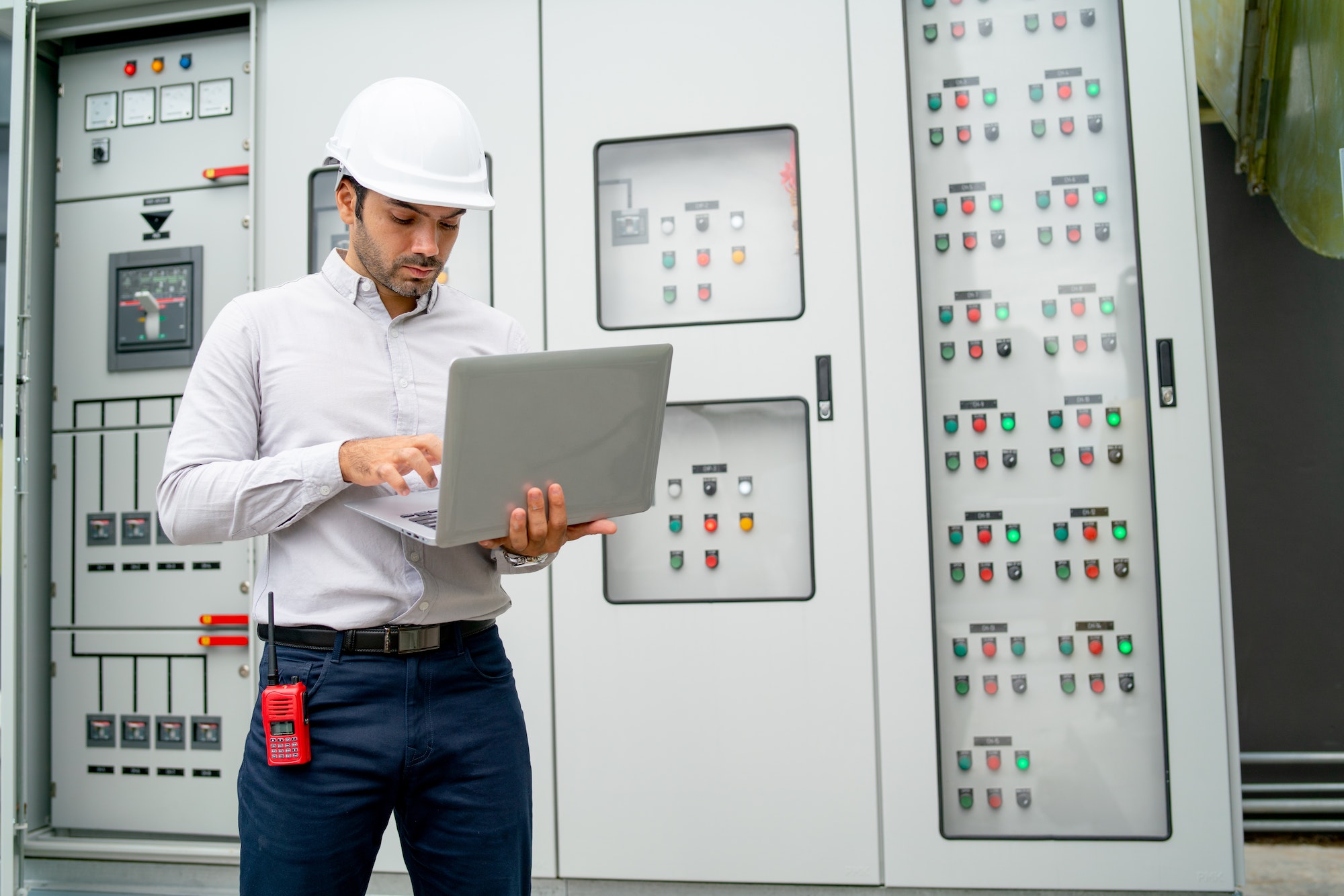 Caucasian engineer man use laptop in front of electrical control panel during process work